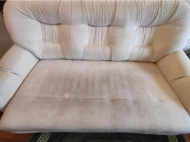 Kremowa sofa przed praniem — na siedzisku szare zabrudzenia i ciemniejsze obwódki wzdłuż przeszyć.