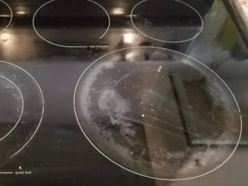 Czarna płyta indukcyjna przed renowacją — matowa, zamglona tafla, wokół prawego pola biały przypalony osad.